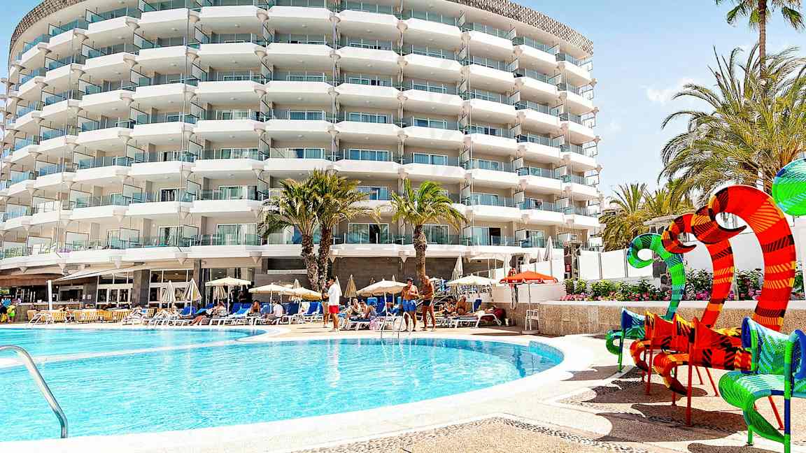 Hotellirakennus parvekkeilla, palmuja ja allasalue. (Tekoälyn luoma teksti)