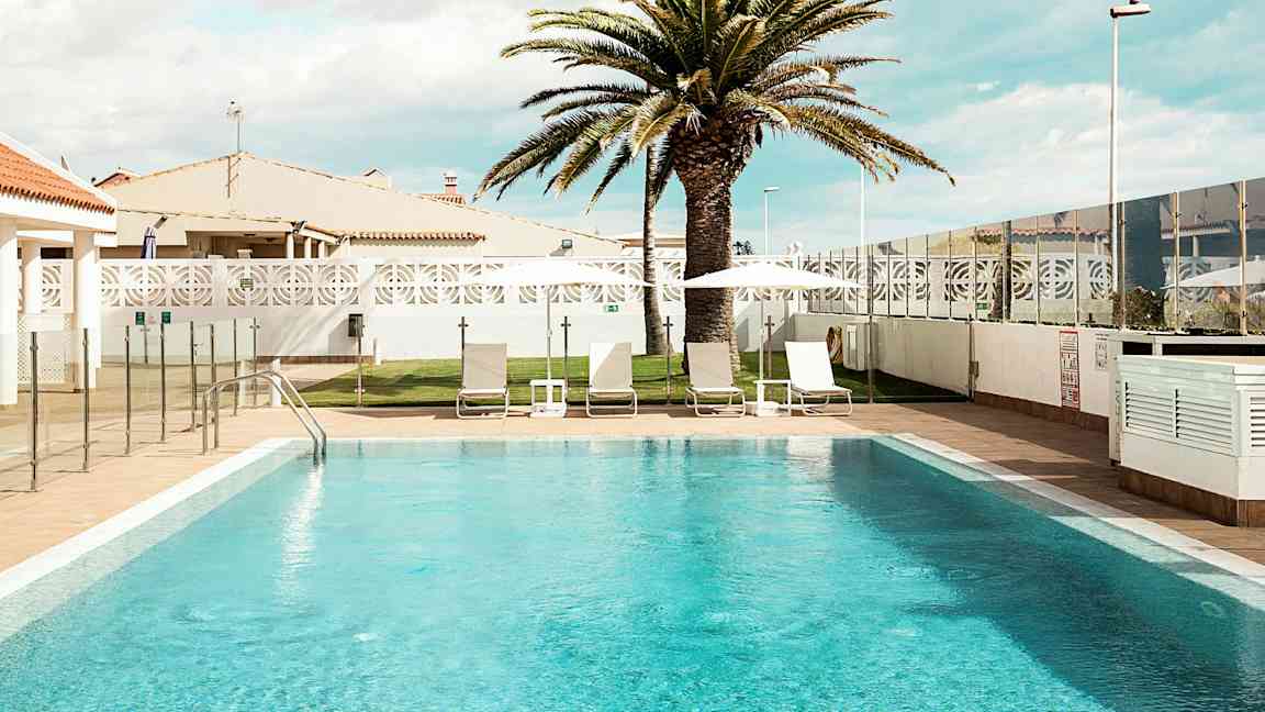 Ulkouima-allas, jossa on aurinkotuoleja ja aurinkovarjoja sekä palmu taustalla. (Tekoälyn luoma teksti)