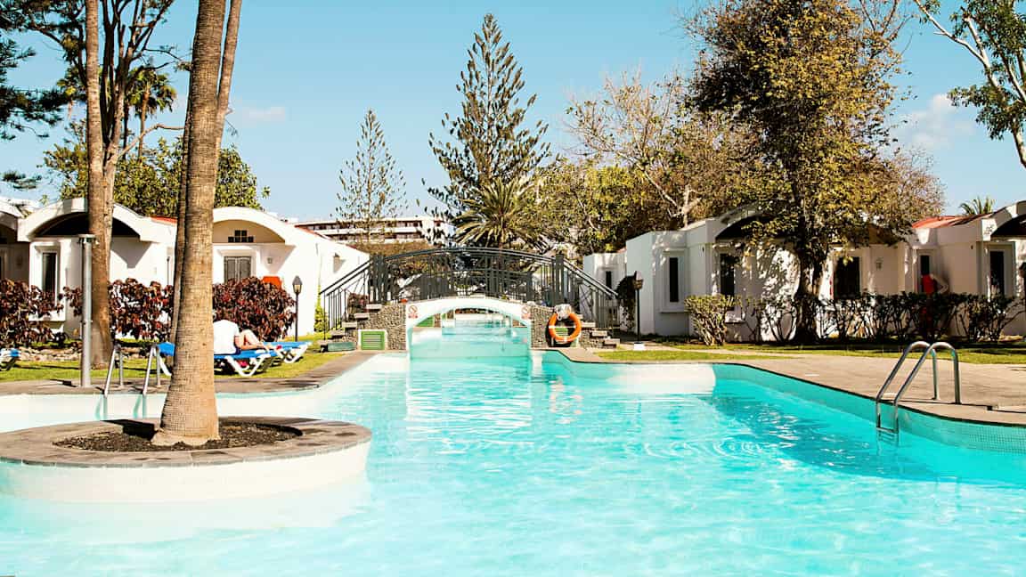 Altaan kirkas vesi ja pieni silta ympäröitynä vehreydellä ja lomamajoilla. (Tekoälyn luoma teksti)