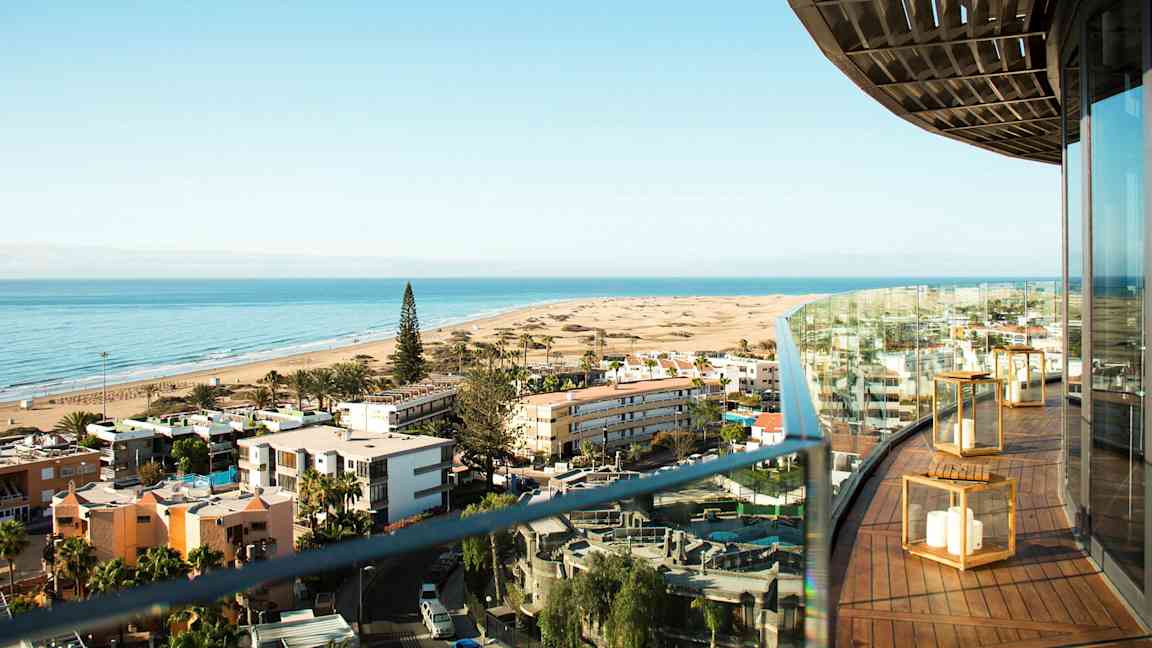 Näkymä rannalle, jossa on rakennuksia ja metsää, nähtynä parvekkeelta. (Tekoälyn luoma teksti)