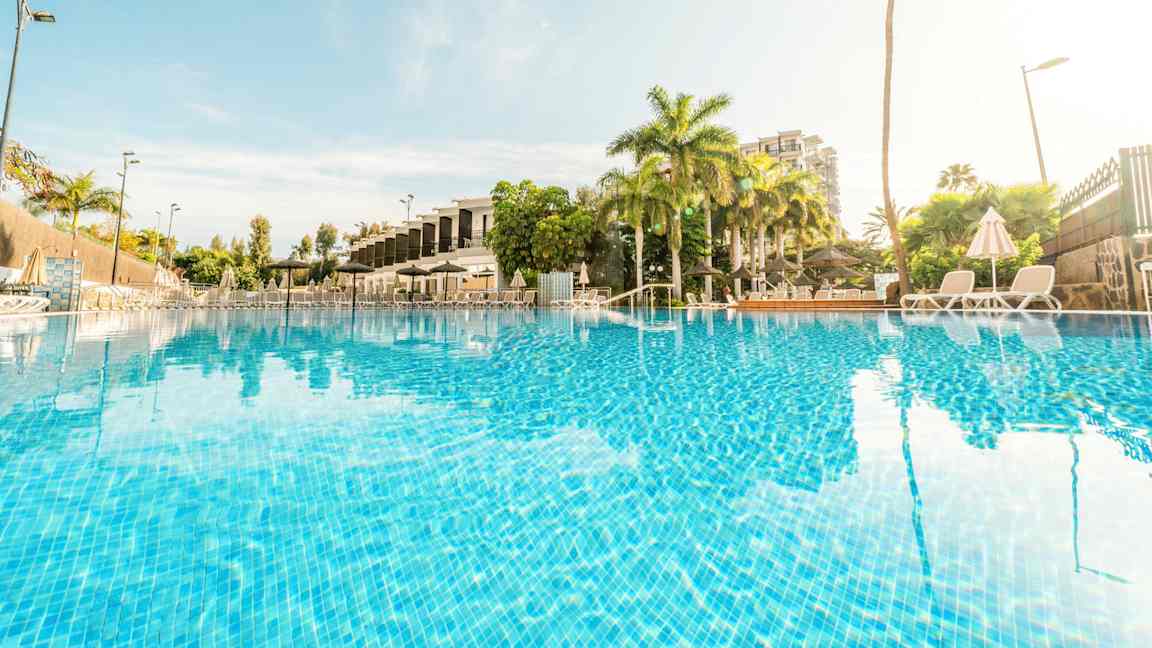 Kuva ulkouima-altaasta, jota ympäröivät palmupuut ja aurinkotuolit. (Tekoälyn luoma teksti)