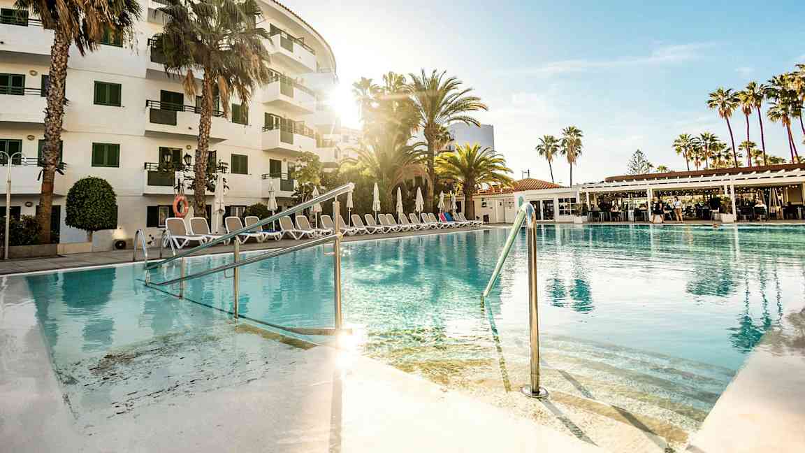 Ulkoallas hotellin edessä, ympärillä palmuja ja aurinkotuoleja. (Tekoälyn luoma teksti)