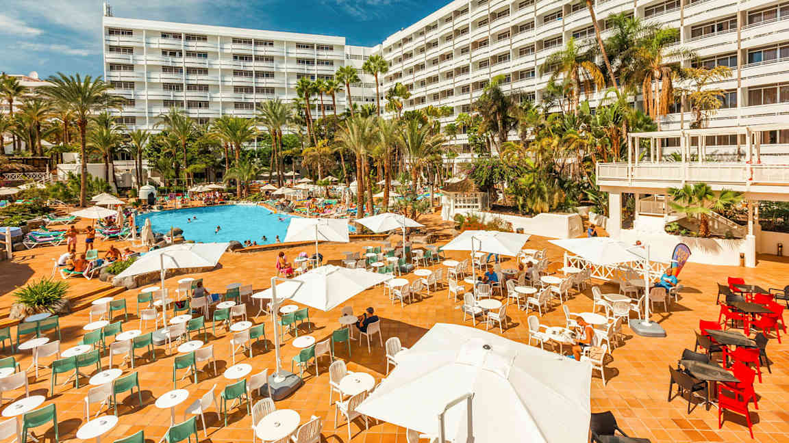 Hotelli, jossa on suuri ulkoterassi, uima-allasalue ja palmuja. (Tekoälyn luoma teksti)