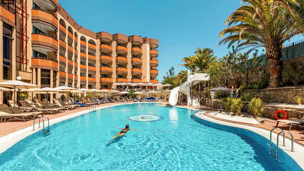 Uima-allas, jossa nainen ui, ympärillä lepotuoleja ja hotelli taustalla. (Tekoälyn luoma teksti)