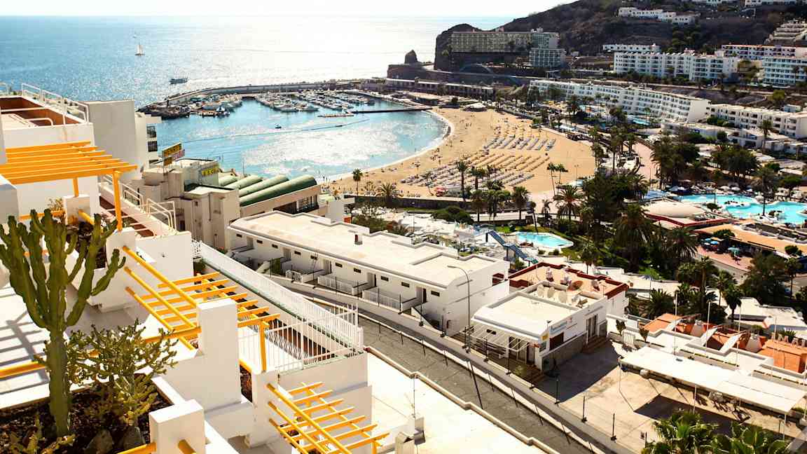 Näkymä rannikkokaupunkiin, jossa on valkoisia rakennuksia, ranta ja pienvenesatama meren äärellä. (Tekoälyn luoma teksti)