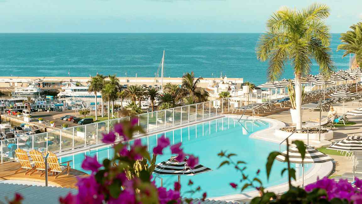 Uima-allas, josta on näkymä merelle ja satamaan. Etualalla on kasveja ja ulkokalusteita. (Tekoälyn luoma teksti)