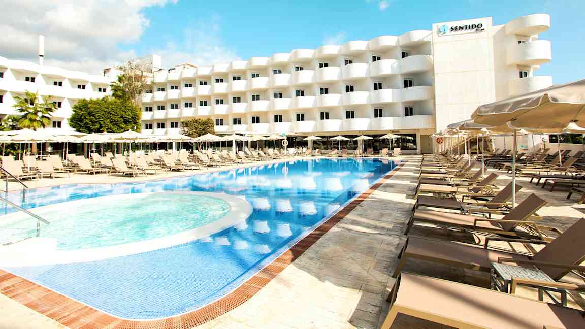 Ulkouima-allas, jota ympäröivät aurinkotuolit ja aurinkovarjot, taustalla monikerroksinen hotelli. (Tekoälyn luoma teksti)