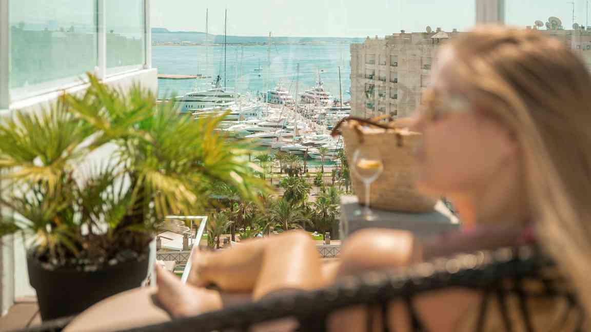 Näkymä veneisiin satamassa, lasiparveke ja vehreitä kasveja etualalla. (Tekoälyn luoma teksti)