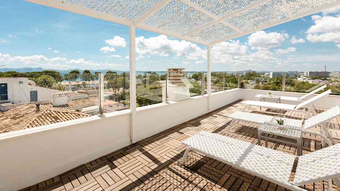 Kattoterassi aurinkotuoleilla ja pöydällä. Terassilla on rei’itetty katos ja lasikaide, josta on näkymä kaupungille ja merelle. (Tekoälyn luoma teksti)
