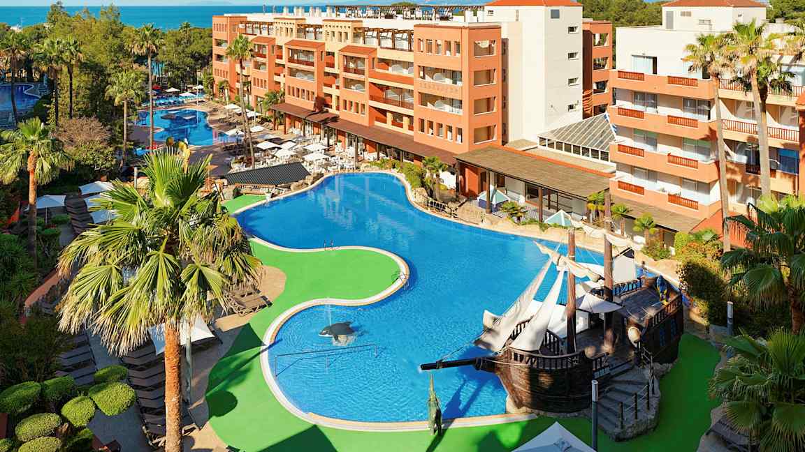 Hotellialue, jossa suuri uima-allas, ympärillä palmuja ja rakennuksia. (Tekoälyn luoma teksti)