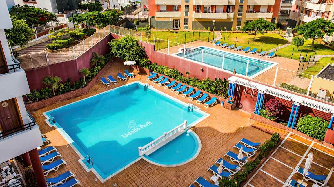 Hotellialue, jossa on kaksi uima-allasta, aurinkotuoleja ja ympäröiviä rakennuksia. (Tekoälyn luoma teksti)