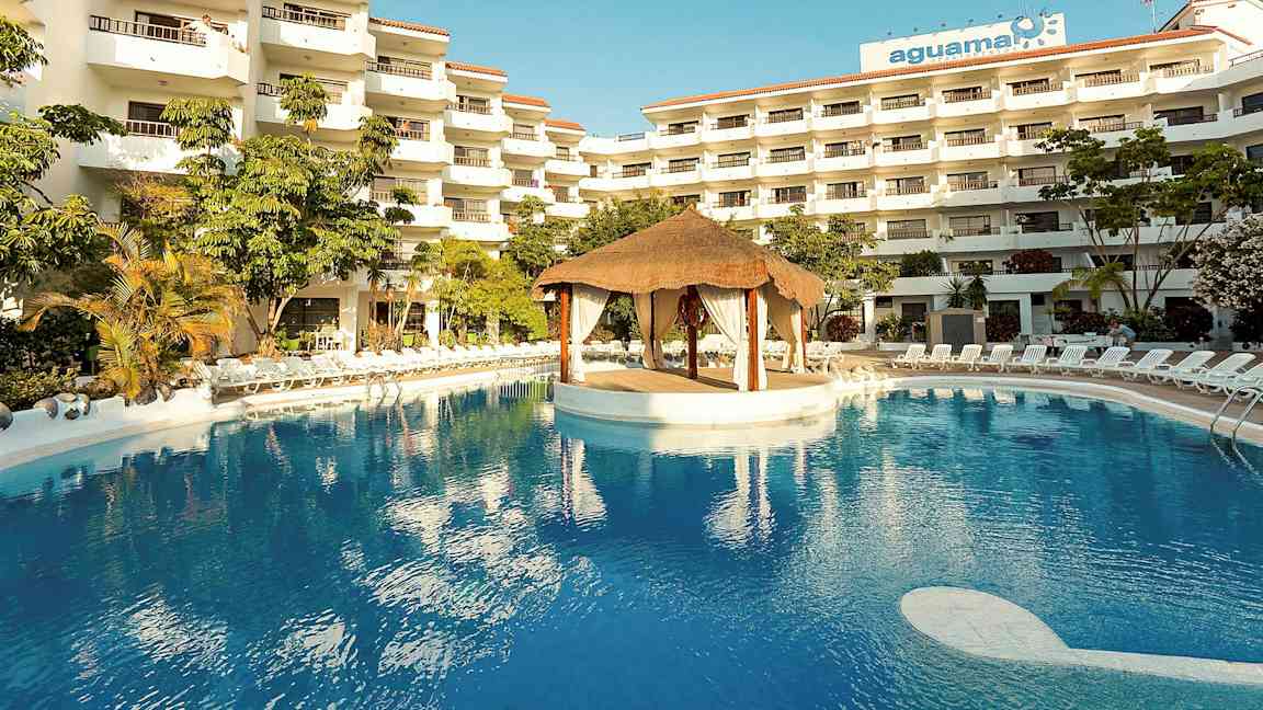 Hotellikompleksi, jossa useita kerroksia, suuri uima-allas ja katkokatosrakennelma altaan keskellä. (Tekoälyn luoma teksti)