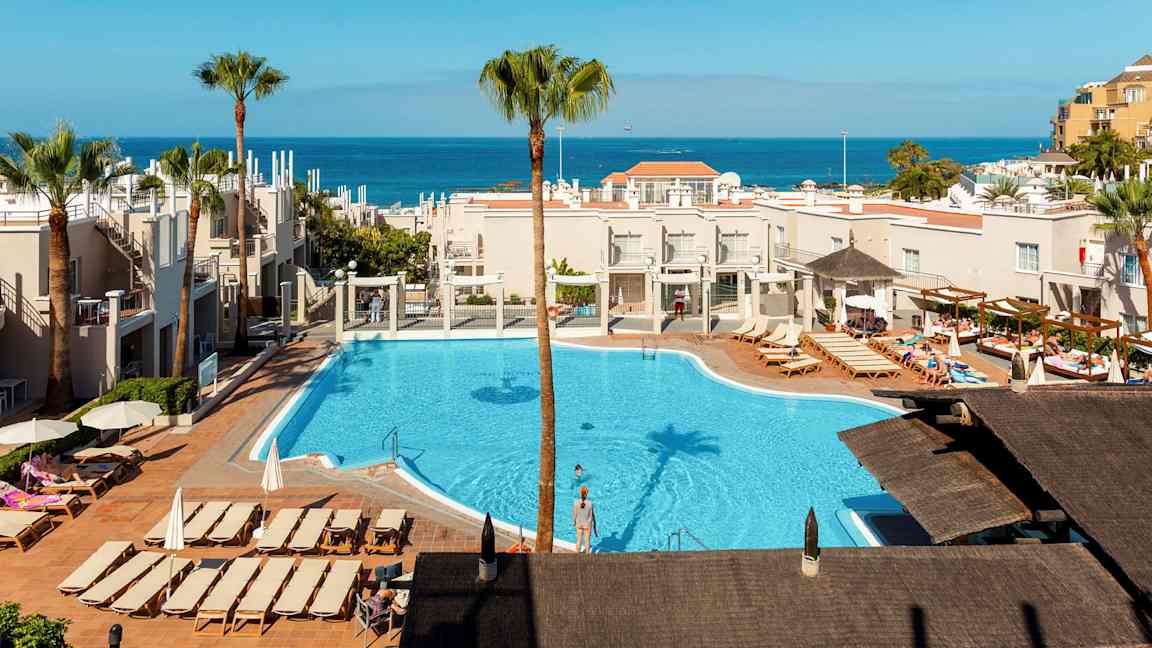 Näkymä hotellialueelle, jossa on uima-allas ja aurinkotuoleja, meri näkyy taustalla. (Tekoälyn luoma teksti)