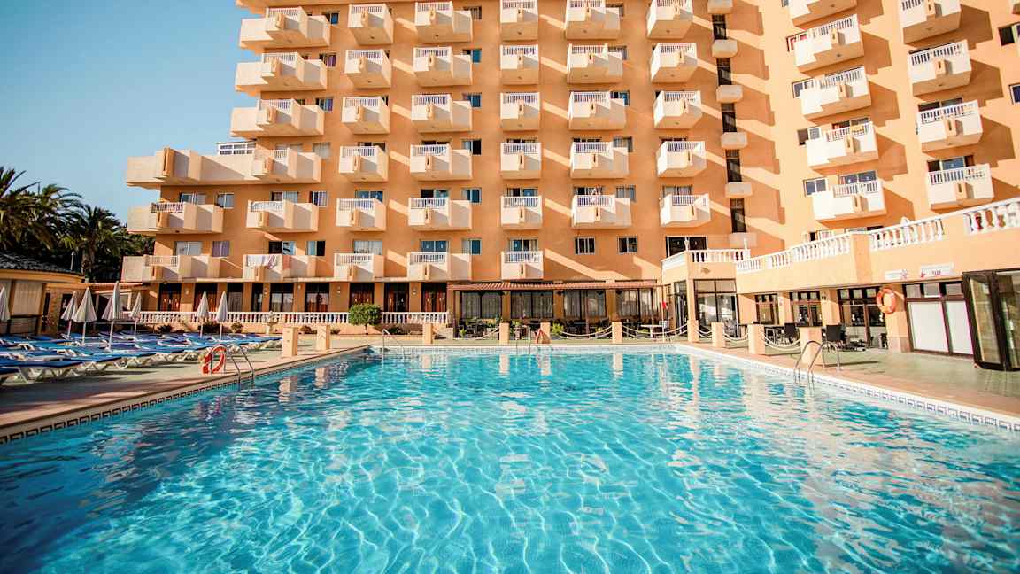 Rakennus, jossa on useita parvekkeita, ja sen edustalla suuri uima-allas. (Tekoälyn luoma teksti)