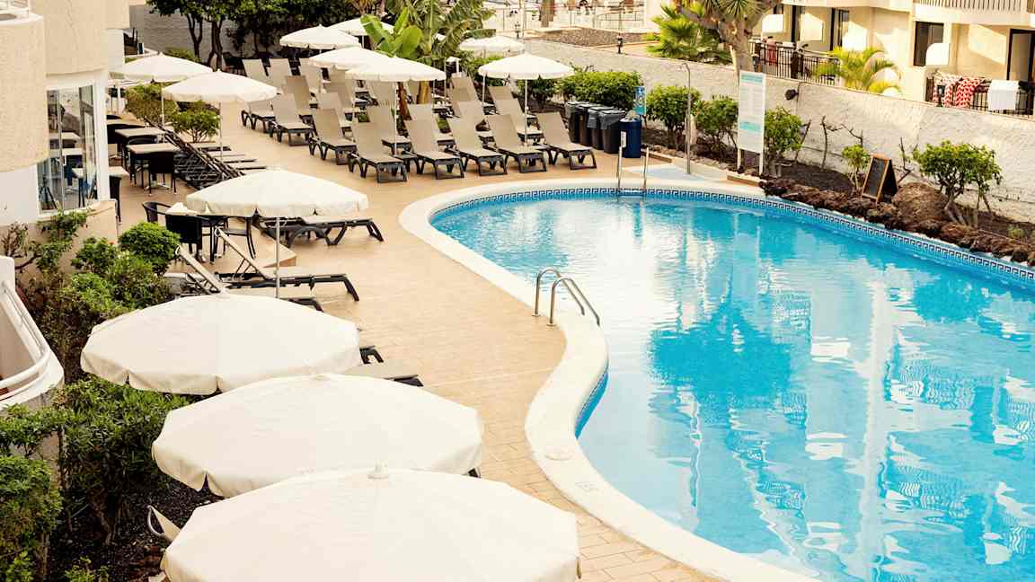 Uima-allasalue aurinkotuoleilla ja varjoilla hotellin vieressä. (Tekoälyn luoma teksti)