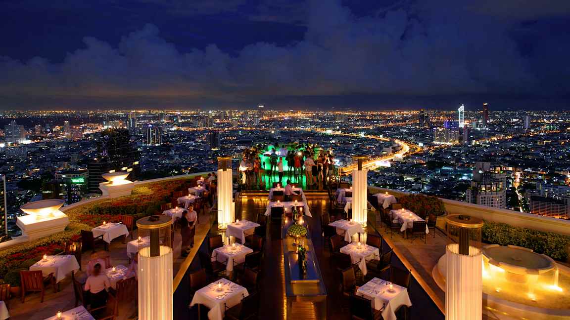 Katuterassiravintola iltavalaistuksessa, jossa on valoisat pöydät ja näkymät kaupunkiin. (Tekoälyn luoma teksti)