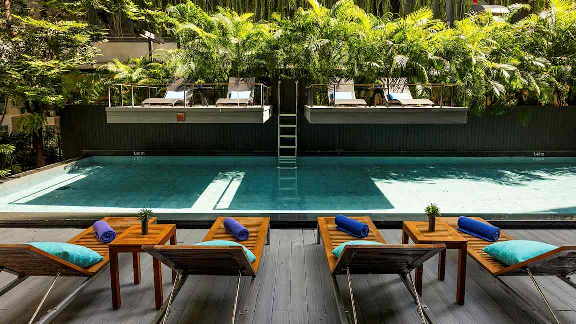 Uima-allas, jonka edessä on aurinkotuoleja ja pöytiä, ympärillä vehreyttä ja palmuja. (Tekoälyn luoma teksti)