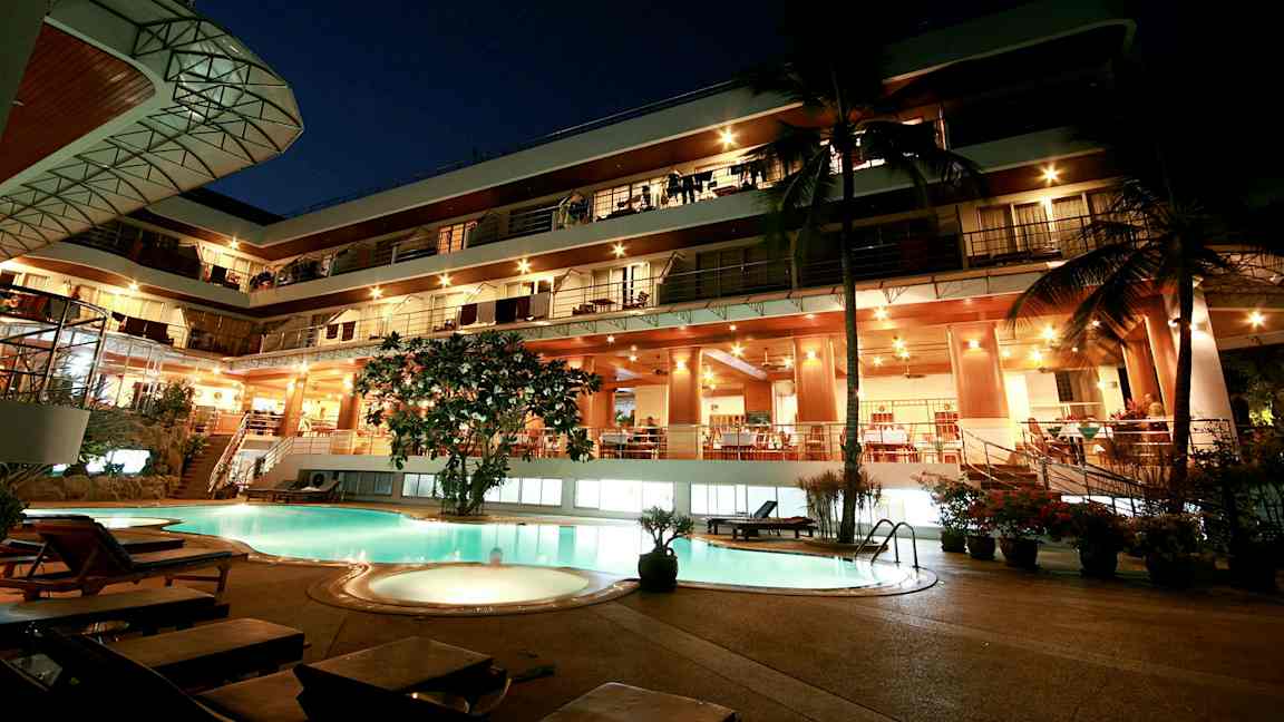 Ilta näkymä monikerroksisesta rakennuksesta, valaistu julkisivu ja uima-allas etualalla. (Tekoälyn luoma teksti)