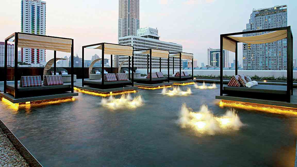 Kuva modernista kaupunkinäkymästä, jossa päivävuoteita sijaitsee matalan altaan yläpuolella, jossa on valoinstallaatioita vedessä. (Tekoälyn luoma teksti)