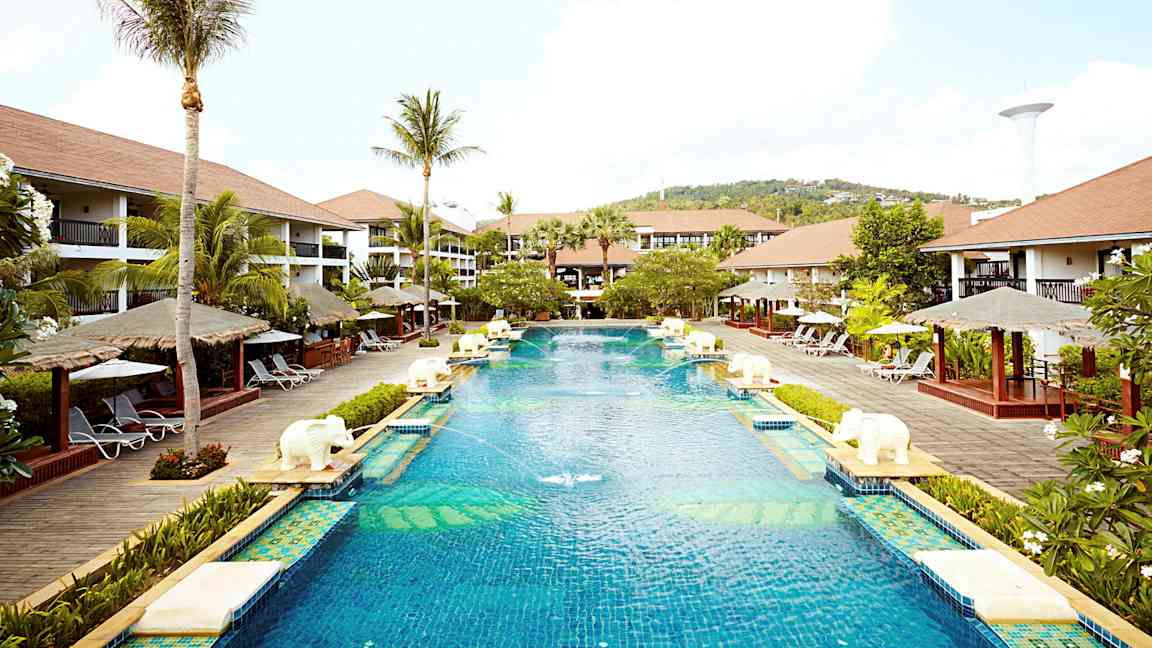 Iso uima-allas lomakeskusalueella, jota ympäröivät palmut, aurinkotuolit ja bungalow-tyyliset rakennukset. (Tekoälyn luoma teksti)