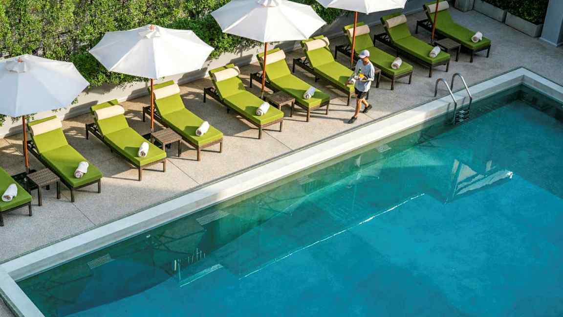 Uima-allas, jonka reunalla aurinkotuoleja ja varjoja, sekä ohi kulkeva henkilö. (Tekoälyn luoma teksti)