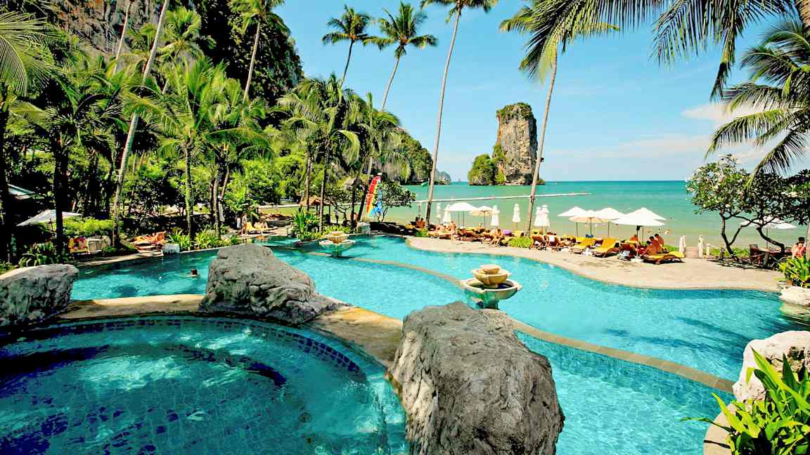 Lomakeskus, jossa uima-allas rannan äärellä, ympäröitynä palmuilla ja upealla merinäköalalla sekä kallio näkyy horisontissa. (Tekoälyn luoma teksti)