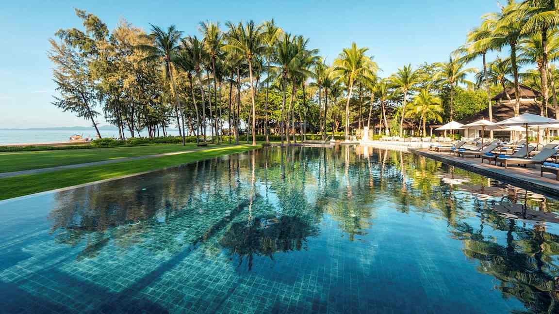 Ulkoallas, jota ympäröivät vehreys ja palmut, näkymä rannalle ja merelle. (Tekoälyn luoma teksti)