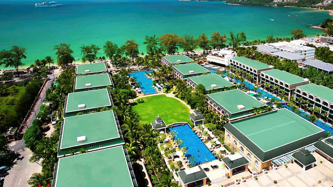 Ilmakuva lomahotellista, jossa on useita rakennuksia vehreyden ja uima-altaiden ympäröimänä lähellä merta. (Tekoälyn luoma teksti)