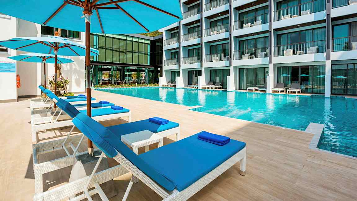 Uima-allas hotellissa, jossa etualalla aurinkotuoleja ja varjoja. (Tekoälyn luoma teksti)