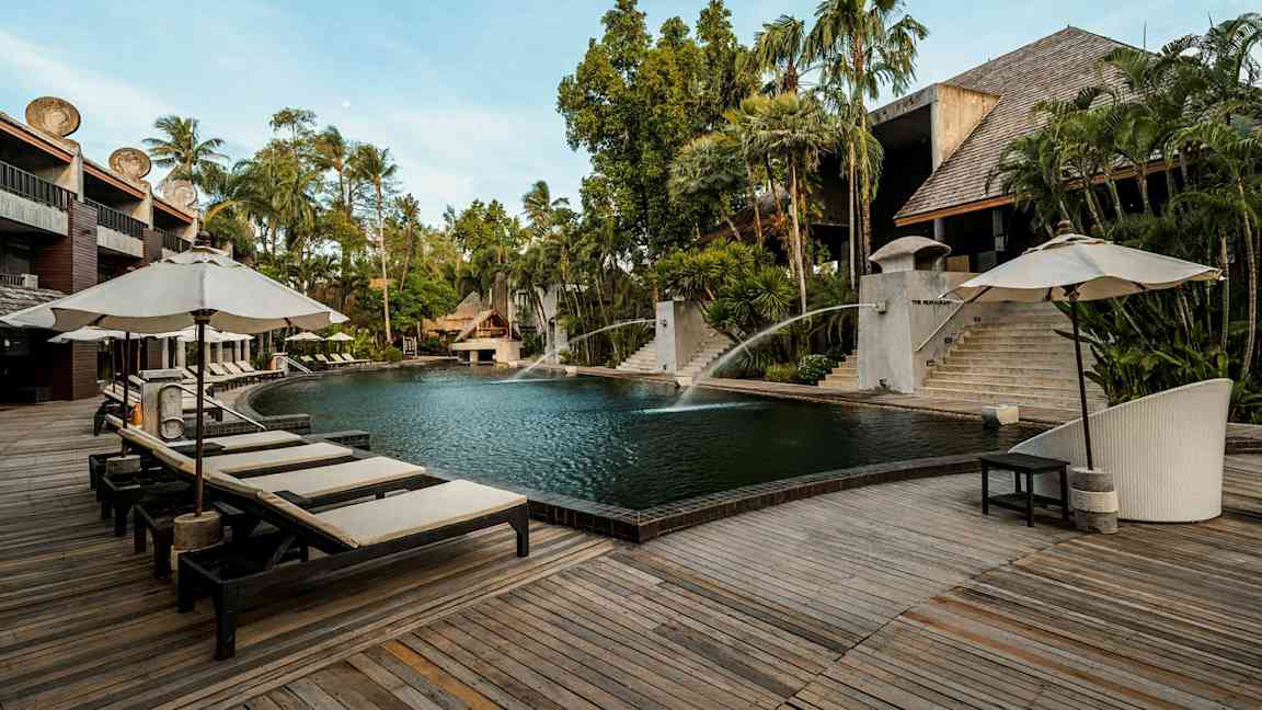 Ulkouima-allas, jonka ympärillä on puuterassi ja aurinkotuoleja varjoineen. Taustalla näkyy vehreää kasvillisuutta ja rakennuksia, joissa on puu- ja kivirakenteita. (Tekoälyn luoma teksti)