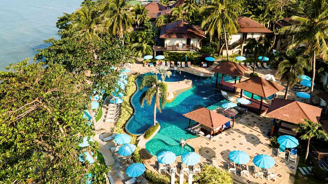 Lomakeskus, jossa on uima-allas, palmuja ja aurinkovarjoja meren äärellä. (Tekoälyn luoma teksti)