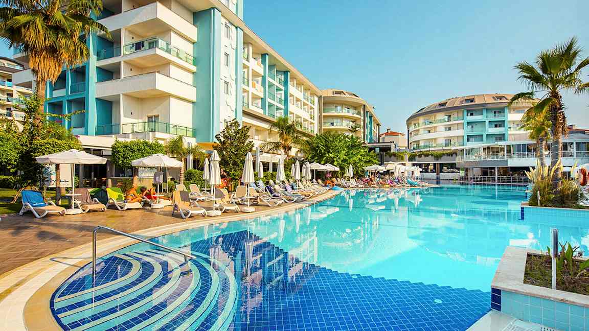 Hotelli rakennettu ulkouima-altaan ympärille, jossa on aurinkotuoleja ja aurinkovarjoja. (Tekoälyn luoma teksti)