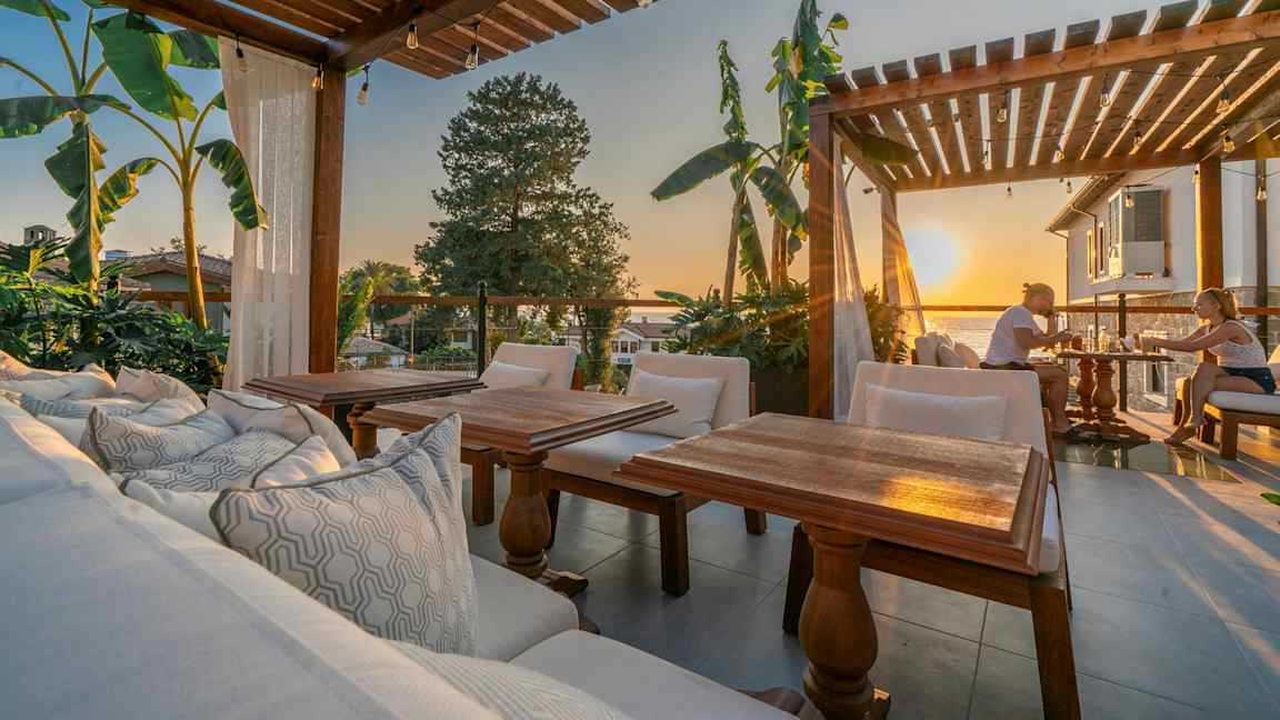 Ulkoterassi, jossa puinen pergola, istuimia ja näkymä auringonlaskuun. (Tekoälyn luoma teksti)