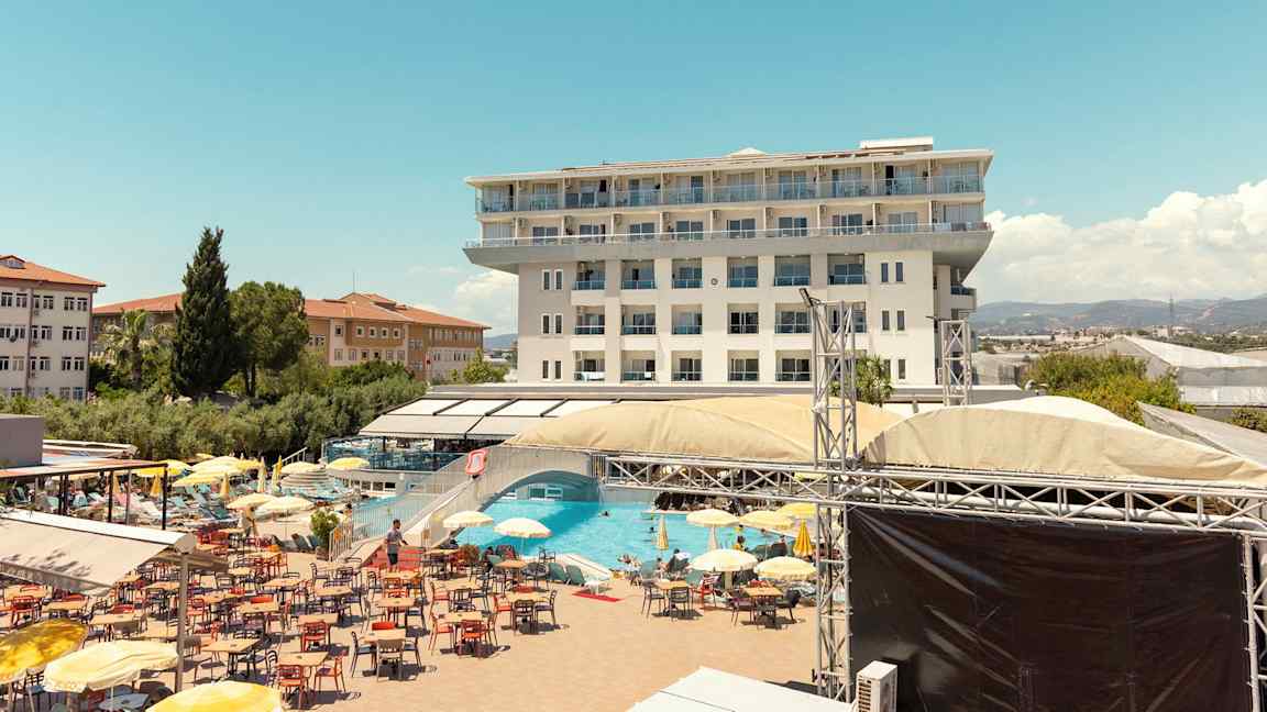 Kuva monikerroksisesta hotellista, uima-allasalueesta aurinkotuoleilla, aurinkovarjoilla ja rentoutumisalueella. (Tekoälyn luoma teksti)