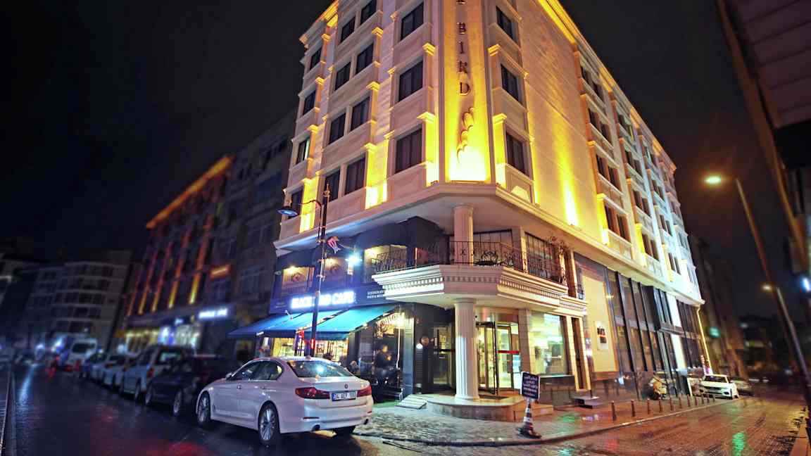 Usean kerroksen rakennus valaistuna illalla, auto parkissa jalkakäytävän vieressä. (Tekoälyn luoma teksti)