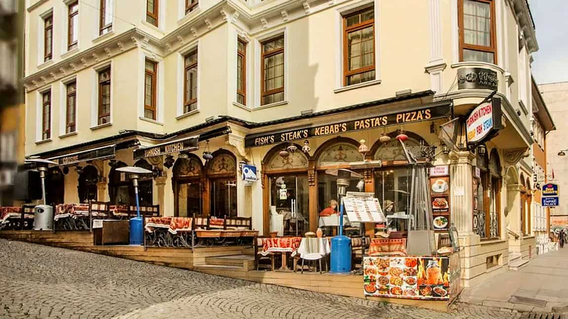 Kadulla sijaitseva rakennus, jossa ravintola ja ulkotarjoilu sekä kyltit ruoasta kuten kebabista ja pizzasta. (Tekoälyn luoma teksti)