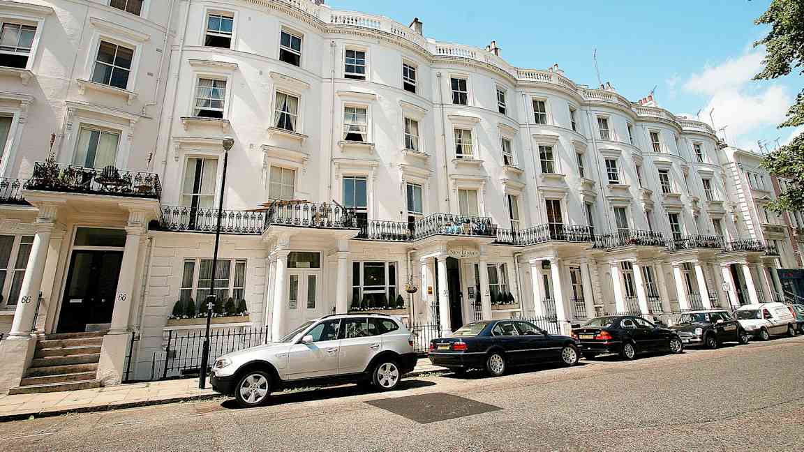 Ryhmä taloja valkoisilla julkisivuilla ja pysäköityjä autoja edessä. (Tekoälyn luoma teksti)