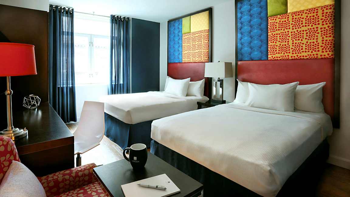 Hotellihuone, jossa on kaksi sänkyä, modernit huonekalut ja koristeellisia yksityiskohtia. (Tekoälyn luoma teksti)