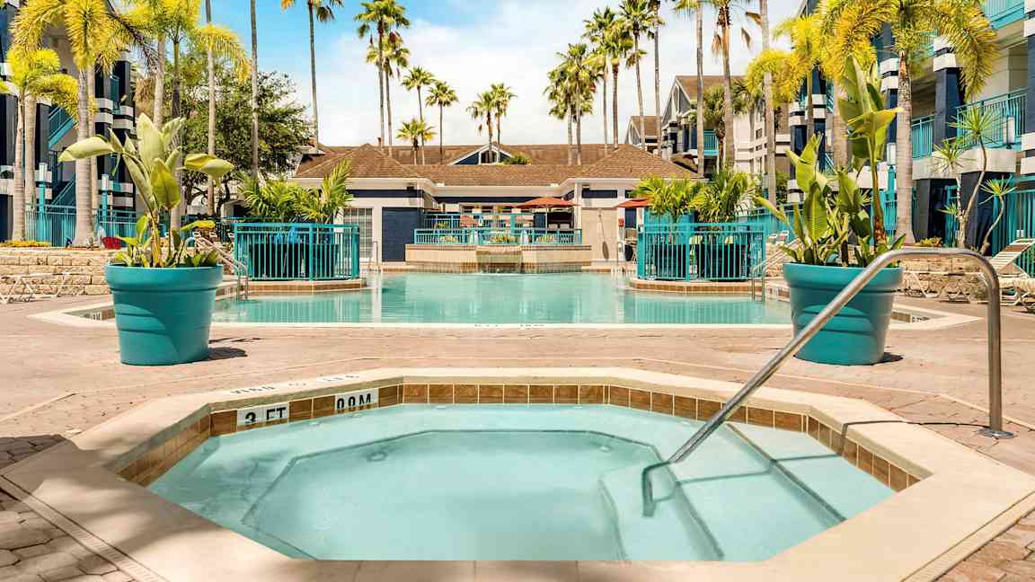 Kuva uima-altaasta, jota ympäröivät aurinkotuolit ja palmut. Etualalla on pienempi poreallas kaiteineen. (Tekoälyn luoma teksti)