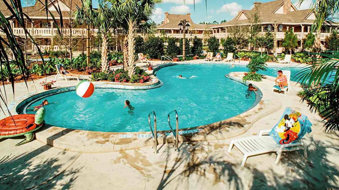 Ulkouima-allas, jonka ympärillä on palmuja ja aurinkotuoleja, joissa ihmiset uivat ja leikkivät vedessä. Taustalla näkyy rakennuksia. (Tekoälyn luoma teksti)