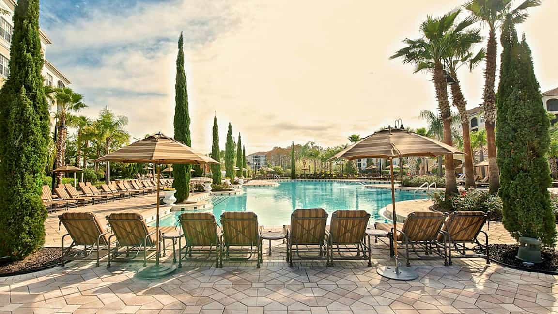 Ulkouima-allas, jossa aurinkotuoleja ja varjoja viihtyisässä ympäristössä, jossa on palmuja ja hyvin hoidettuja alueita. (Tekoälyn luoma teksti)