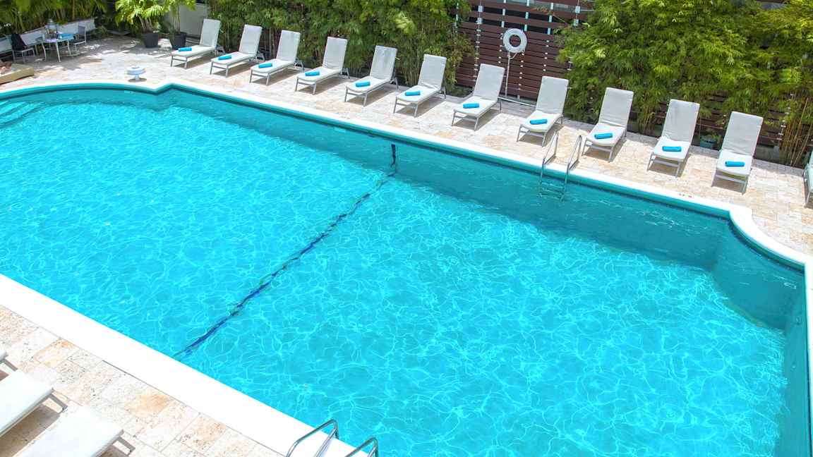 Uima-allas, jota ympäröivät aurinkotuolit ja vehreys. (Tekoälyn luoma teksti)