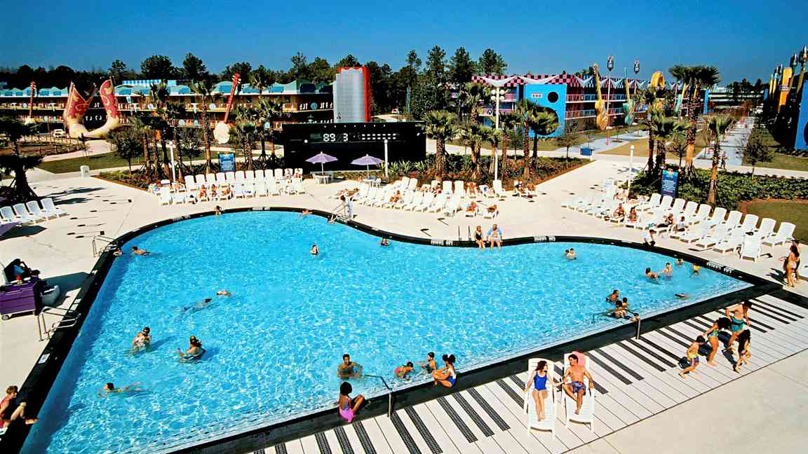 Uima-allas, jota ympäröivät aurinkotuolit lomakohteessa. Taustalla rakennuksia ja koristuksia. (Tekoälyn luoma teksti)