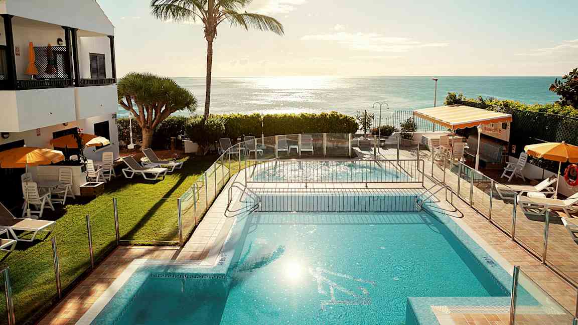 Ulkouima-allas aurinkotuoleineen ja varjoineen, taustalla meri. (Tekoälyn luoma teksti)