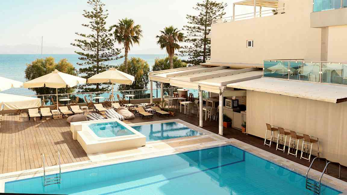 Hotellialue, jossa on uima-allas, aurinkotuoleja ja varjoja meren äärellä. (Tekoälyn luoma teksti)