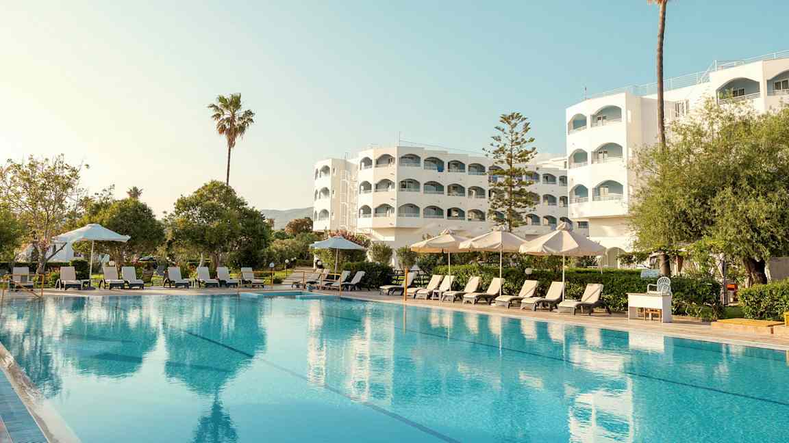 Hotellirakennus uima-altaan kanssa, aurinkotuoleja ja aurinkovarjoja etualalla. (Tekoälyn luoma teksti)