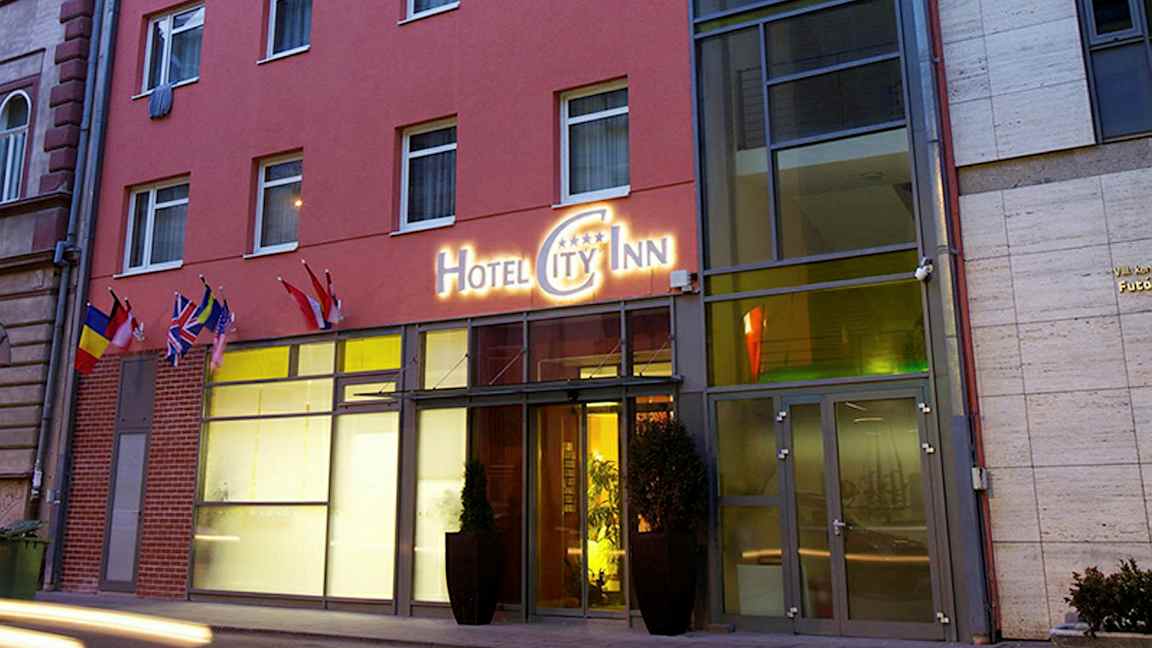 Hotellirakennuksen ulkopuolella kyltti, jossa lukee "Hotel City Inn", sekä useita lippuja sisäänkäynnin luona. (Tekoälyn luoma teksti)