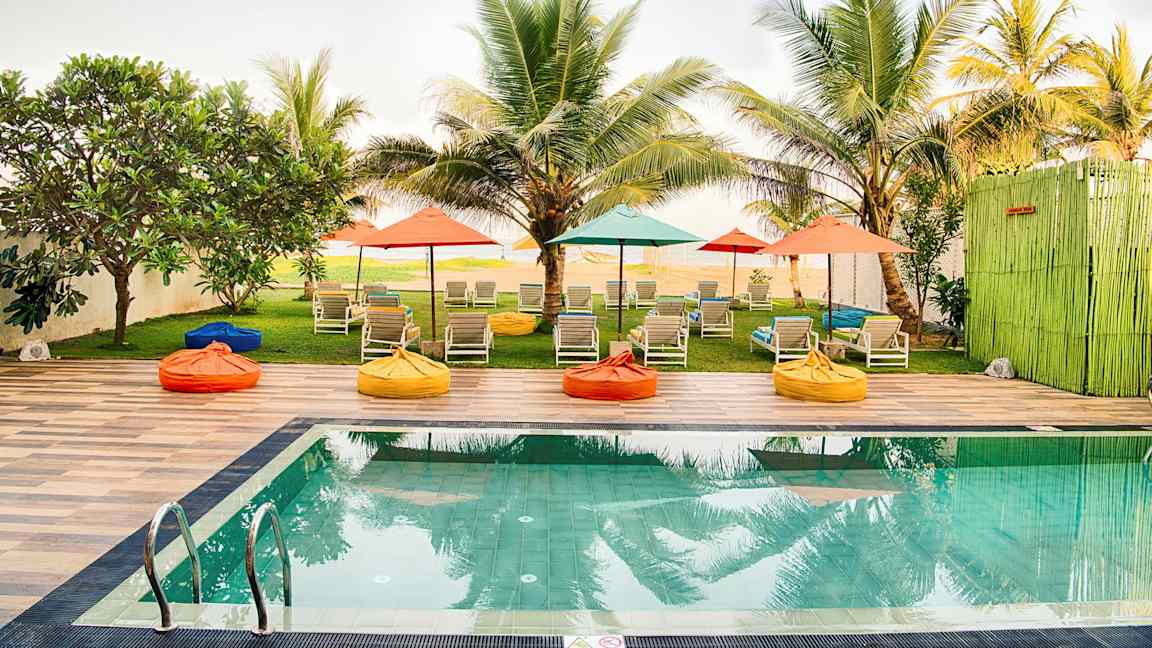 Uima-allas, jossa on aurinkotuoleja ja värikkäitä varjoja palmujen ympäröimässä puutarhassa. (Tekoälyn luoma teksti)