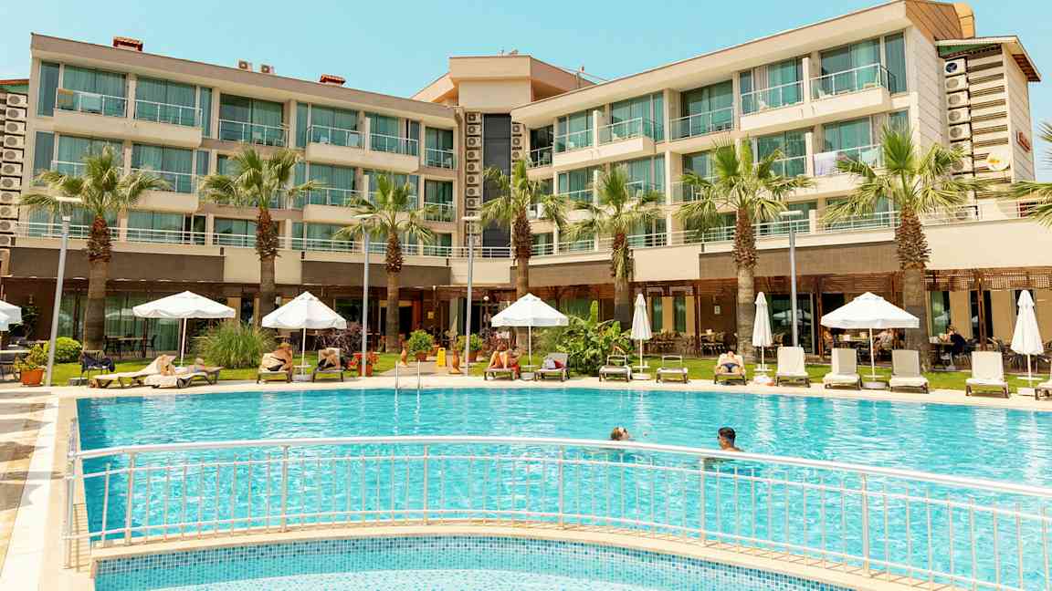 Hotellinäkymä uima-altaalla, aurinkotuoleilla ja varjoilla. (Tekoälyn luoma teksti)