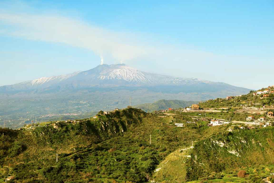 Vehreä maaseutu mäkisessä maastossa, taustalla vuori lumihuippuineen. (Tekoälyn luoma teksti)